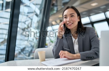 Young busy chinese business woman talking on phone working in modern office. Asian businesswoman company sales client manager wearing suit making call on cellphone sitting at workplace. Royalty-Free Stock Photo #2187470267