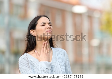 Stressed woman suffering sore throat standing in the street Royalty-Free Stock Photo #2187475931