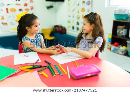 Adorable happy girls in preschool sharing their color pencils while coloring and learning in the classroom Royalty-Free Stock Photo #2187477521