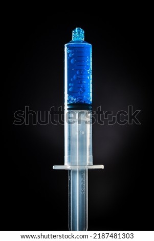 Closeup photo of a medical syringe filled with a blue liquid with bubbles over a black background