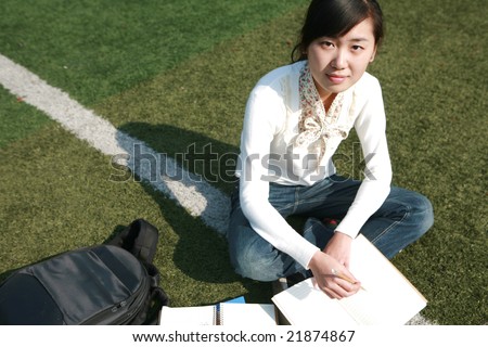 young asian girl holding books sitting on grassland