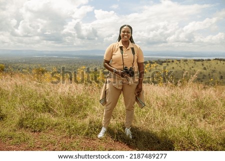 Smiling female guide holding binoculars and posing against the backdrop of the savannah in Africa Royalty-Free Stock Photo #2187489277