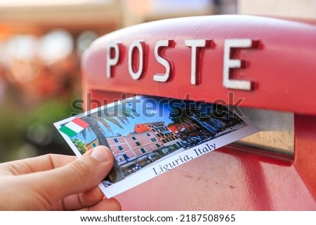 Male send a postcard to a red mailbox in Liguria, Italy. The postcard shows a Liguria coast, Sestri Levante city 