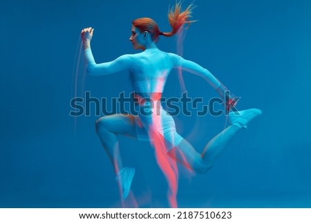 Running workout. Athlete woman runs in air on blue studio backdrop. Long exposure. Motion blur. Sports club advertising Royalty-Free Stock Photo #2187510623