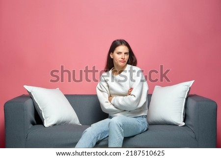 Offended grumpy girl sitting on sofa with crossed arms in studio. Skeptical woman looking at camera with suspicion Royalty-Free Stock Photo #2187510625