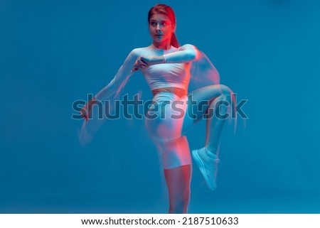 Fitness girl rasing hips, doing warm up exercise for legs on blue backdrop. Long exposure, motion blur. Sports workout Royalty-Free Stock Photo #2187510633