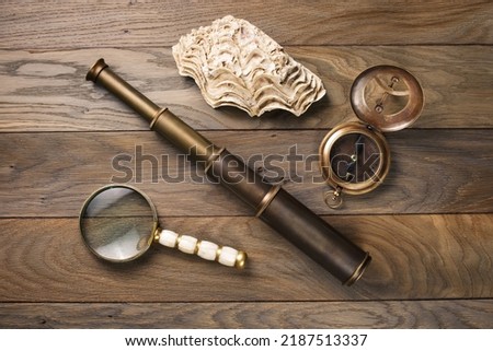 Old vintage compass, magnifying glass, ancient spyglass, shell on oak table. Travel, geography, navigation concept. Royalty-Free Stock Photo #2187513337