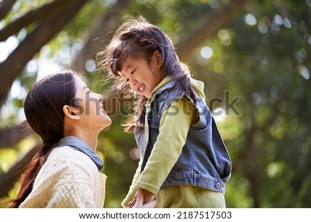 young asian mother sitting on grass in park having a pleasant conversation with cute daughter Royalty-Free Stock Photo #2187517503