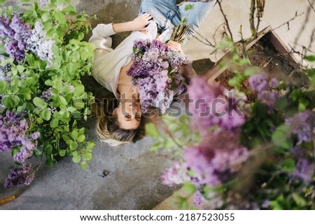 view top. an attractive blonde in a white shirt and jeans on the floor with lilac flowers. profession of a florist. fragrances and perfumes for the home. femininity and tenderness. feminine beauty. Royalty-Free Stock Photo #2187523055