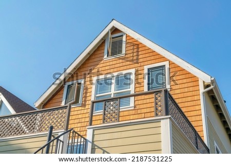 Low angle view of a house with wood shingles wall sidings and side hinged windows. Home exterior with wooden railings on the veranda and metal handrails on the stairs at the front. Royalty-Free Stock Photo #2187531225