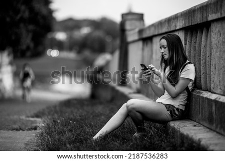 A girl taiping text on her cell phone outdoors. Black and white photo. 