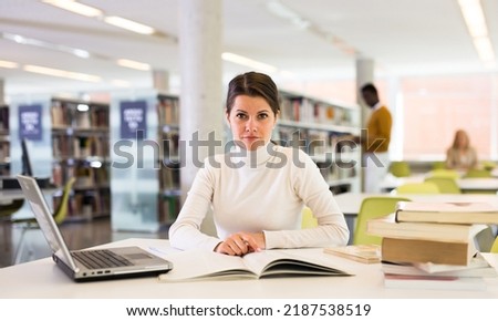 Adult female student with laptop and books in public library. High quality photo