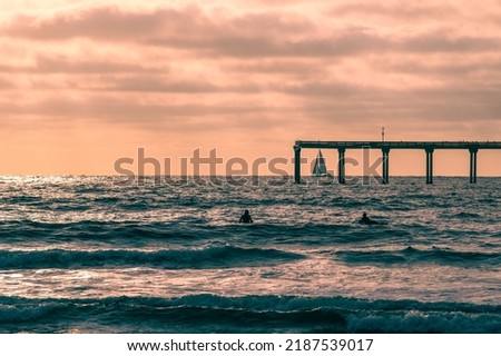 San Diego colorful sunset with sail boat under Ocean Beach pier and surfers in the water Royalty-Free Stock Photo #2187539017
