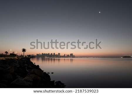 Early morning downtown skyline cityscape of San Diego California with a palm tree and crescent moon and a reflection on calm water