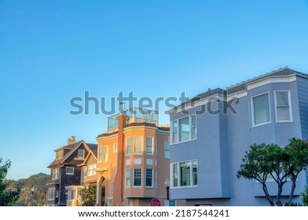 Large residential house buildings near the street lamps and stop sign in San Francisco, California. There are houses with wood shingle siding, roof deck, and picture windows against the clear sky.
