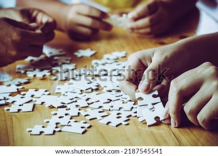Hands of a person little child and parent playing jigsaw puzzle piece game together on wooden table at home, concept for leisure with family, play with children's development, education and fun.