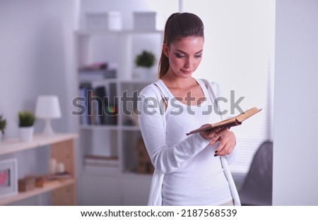 Attractive businesswoman standing near wall in office with book.