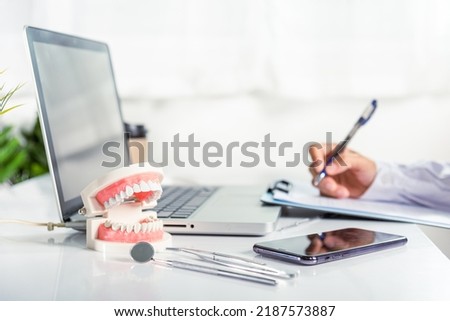 Oral dental. Dentist doctor in uniform writing information of patient in paperwork checklist on clipboard on desk office, teeth model, X-ray on laptop screen, prescription medical dental healthcare