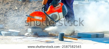 Concrete cutting machine. A worker with a circular saw in the process of cutting, sawing granite, concrete tiles. New construction work on the repair, reconstruction of the pavement, road.