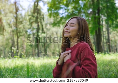 Portrait image of a young woman with closed eyes putting hands on her chest in the park Royalty-Free Stock Photo #2187583049