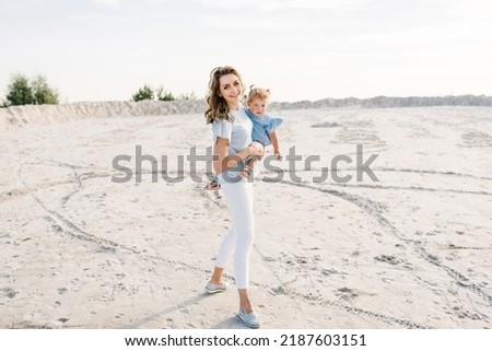 Mother and daughter walk on the sand together outdoors. Mom holding and hugging a little kid girl in nature. Girls walking on the sandy beach. Mother's day. Family and childhood concept.