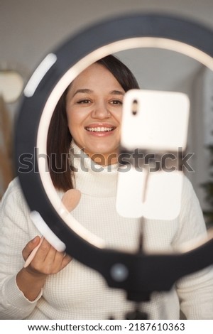 Vertical portrait of plus size female beauty blogger making tutorial video on mobile phone through the light ring lamp