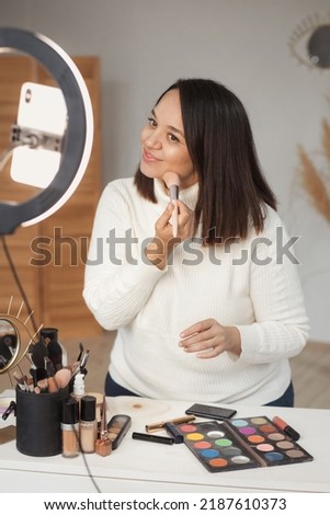 Portrait of plus size woman live streaming cosmetics product review in home studio with light ring. Vlogger job.