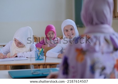 Group of Muslim school children sitting at the school desk in the classroom during class listening to a teacher.