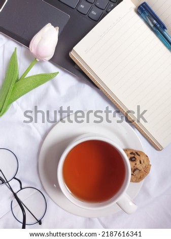 Break time concept. A cup of tea. Completed with laptop, blank book,blue pen, glasses, tulip flower and white plate.