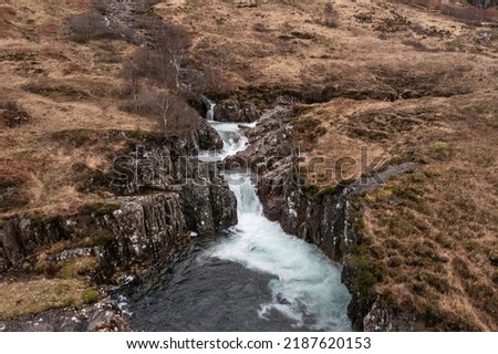 Beautiful aerial drone landscape image of vibrant River Coe flowing beneath snowcapped mountains in Scottish Highlands 