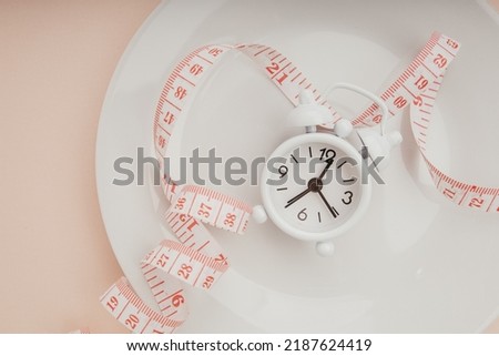 Plate with measuring tape and alarm clock on pink background close-up. Concept diet, healthy food and meal plan.