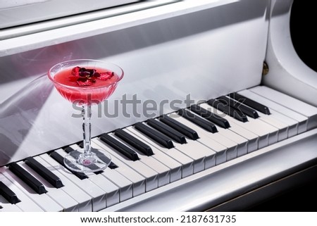 Cocktail with dried strawberries and a flower petal in a glass standing on a piano keyboard