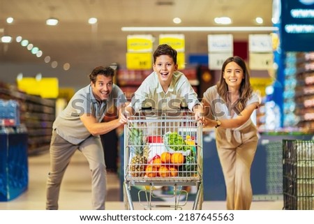 Happy family with child and shopping cart buying food at grocery store or supermarket Royalty-Free Stock Photo #2187645563
