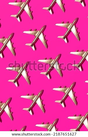Gold plated plane toys arranged in creative summer holiday pattern on neon pink background.  Royalty-Free Stock Photo #2187651627
