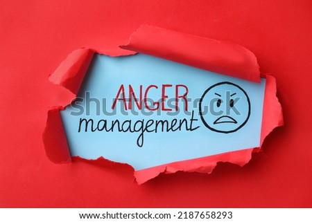 Text Anger Management and drawn angry face on light blue background, view through torn red paper Royalty-Free Stock Photo #2187658293