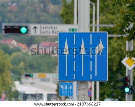 Rectangle blue road sign with three white arrows, two straight ahead and one to the right, attached to a metal pole