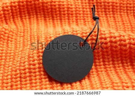 Circle shaped tag with space for text on orange knitted background, closeup