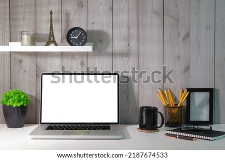 Home office desk with laptop, coffee cup, picture frame and stationery on white table.