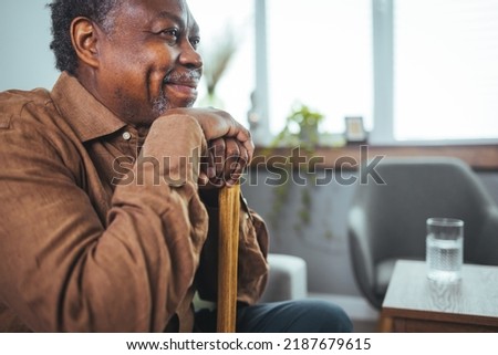 Shot of a senior man looking thoughtfully out of a window at home. Positive African American senior grandfather with grey hair and beard sitting at home. Elderly man sitting alone at home Royalty-Free Stock Photo #2187679615