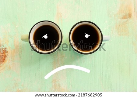 Top view image of coffee cup and sad face. Metaphor for sadness or unhappy emotions