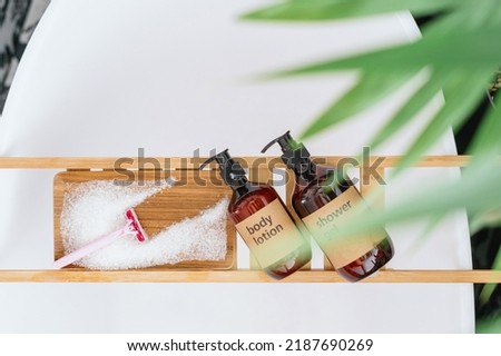 top view of body lotion and shower gel in dispenser bottles, razor and sea salt on wooden caddy on bath or cosmetics products for pampering at home bathtub Royalty-Free Stock Photo #2187690269