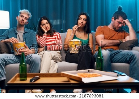 Friends sitting on the couch and watching a boring movie together on TV