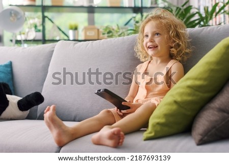 Happy smiling child watching TV at home alone and unsupervised, she is holding the remote control