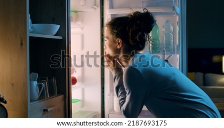 Woman looking in the fridge late at night, she is searching for a snack Royalty-Free Stock Photo #2187693175