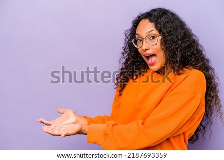 Young hispanic woman isolated on purple background holding a copy space on a palm.