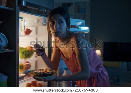 Hungry woman looking in the fridge and eating delicious pastries at night, she is breaking her diet Royalty-Free Stock Photo #2187694803