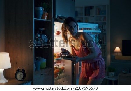 Hungry woman looking in the fridge and eating delicious pastries at night, she is breaking her diet Royalty-Free Stock Photo #2187695573