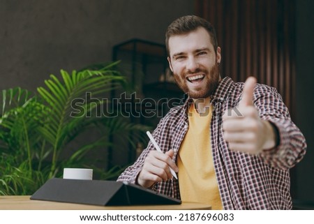 Young man graphic designer he wear shirt hold work use write draw stylus pc pen show thumb up sit at table in coffee shop cafe relax rest in free time indoors Freelance mobile office business concept.