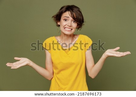 Young woman she 20s wear yellow t-shirt shrugging shoulders looking puzzled, have no ideastanding questioned and unaware, I don't know, why spread hands isolated on plain olive green khaki background Royalty-Free Stock Photo #2187696173