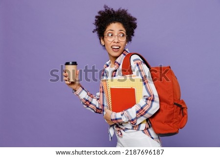 Young side view disappointed sad girl woman of African American ethnicity teen student in shirt backpack hold takeaway delivery craft paper brown cup coffee to go isolated on plain purple background.